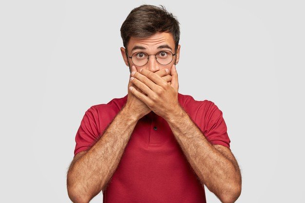 young-emotional-man-posing-against-white-wall-covers-mouth-with-hand_273609-20267