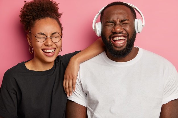overjoyed-afro-american-couple-have-fun-listen-favorite-music-headphones-giggle-something-positive-wear-black-white-clothes-enjoy-spending-time-together-isolated-pink-wall